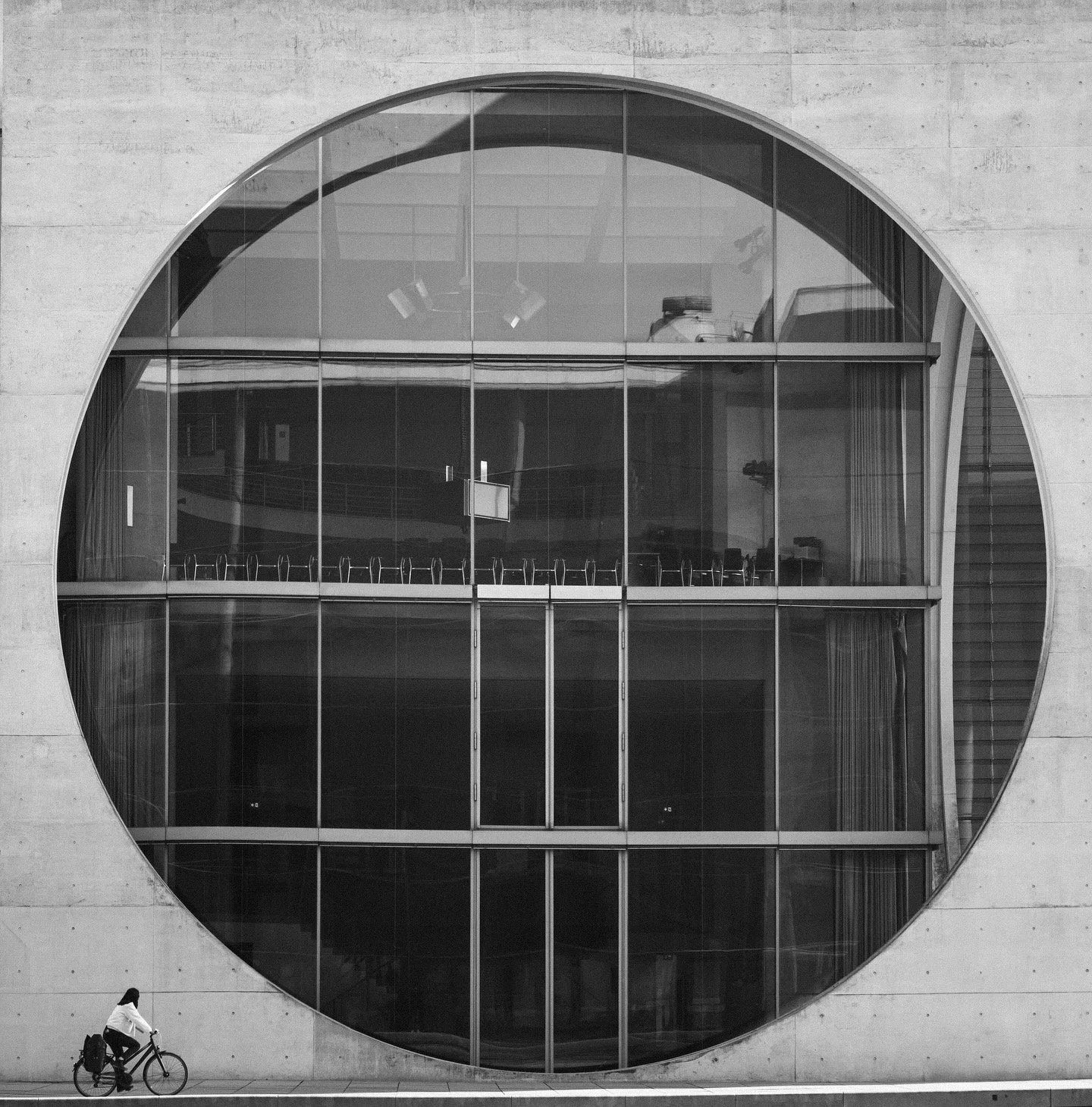 A cyclist riding past a large circular window on a concrete building.