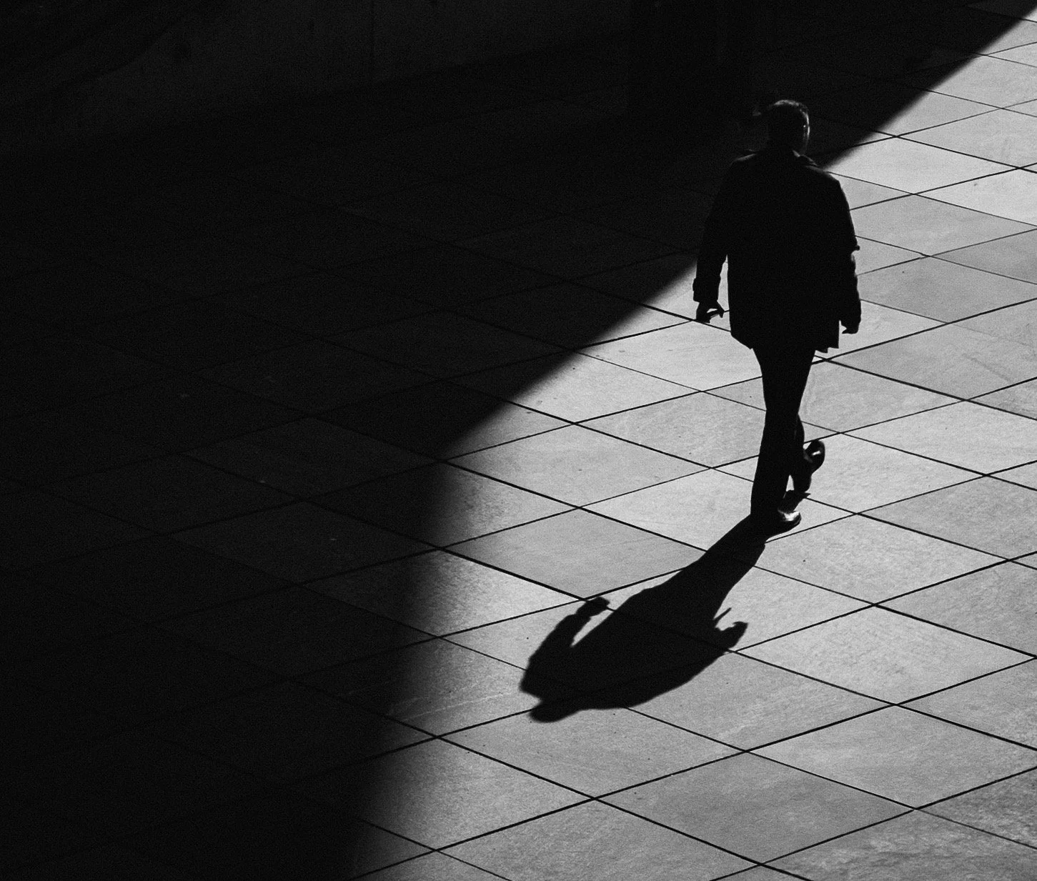 A person walking alone on tiled ground, casting a long shadow.