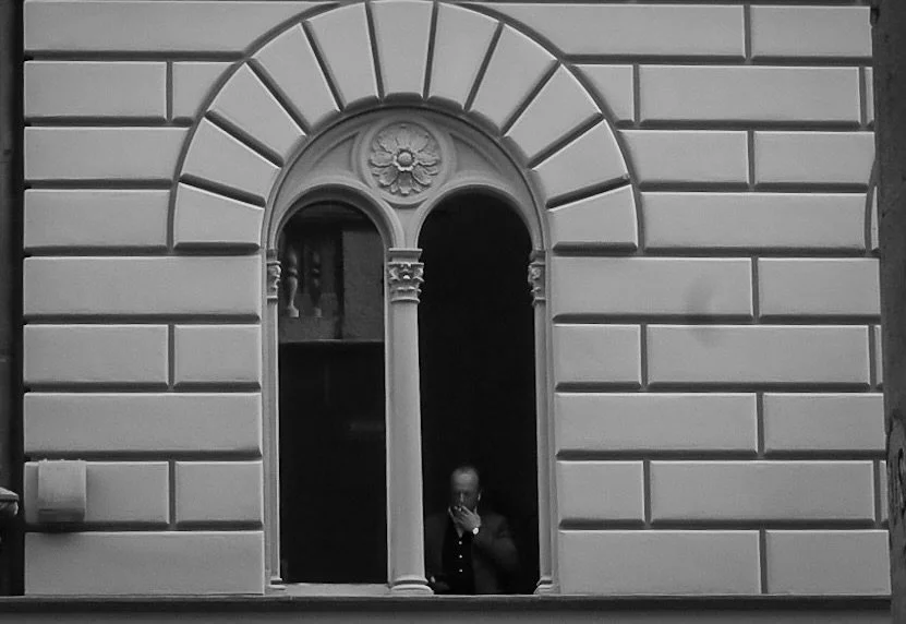 A man taking a selfie in a mirror window on a building with ornate architecture.